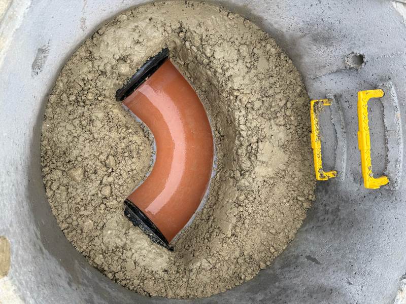 Looking down into a precast concrete manhole: a clay bend bedded in concrete benching, with yellow step irons
