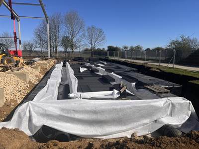 Attenuation tank crates on an impermeable membrane being wrapped in geotextile, with the steel frame and plant behind