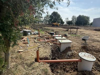 Drainage inspection chambers and orange pipework being installed in an open trench, with the new clad building at the edge of the site