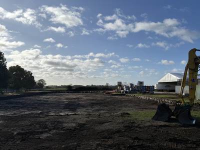 A cleared and stripped site, levelled and ready for the next stage of works, with an excavator bucket in the foreground