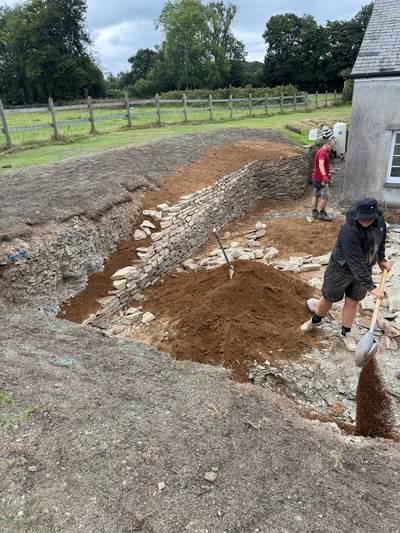 Crew building a dry stone retaining wall into the slope and backfilling behind it