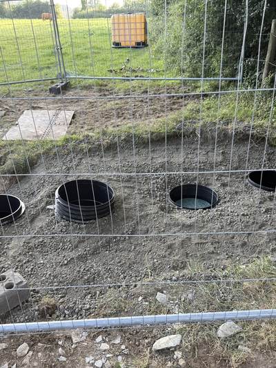 A new drainage field with soakaway chambers bedded in gravel, behind temporary site fencing
