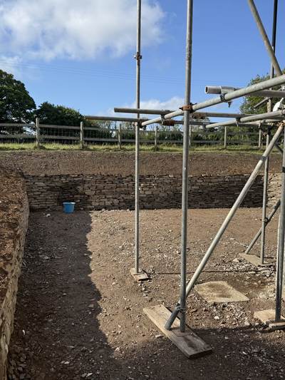 Finished dry stone retaining walls cut into a sloping garden beside a rendered house, with scaffolding against the house
